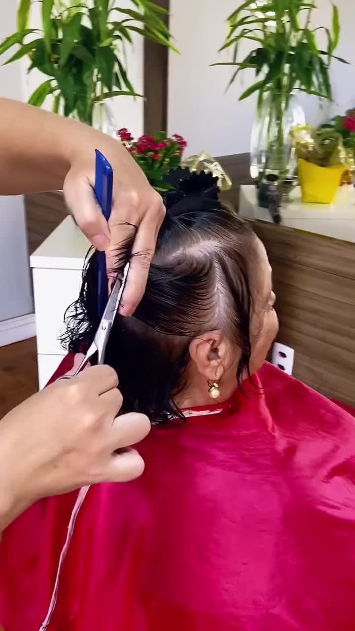 Corte de cabelo em andamento no salão, cliente com capa vermelha